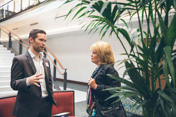 a male students speaks with a female professor next to a palm tree